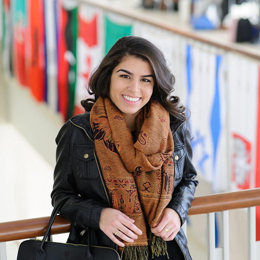 International student stands in front of flags on balcony in Campus Center.